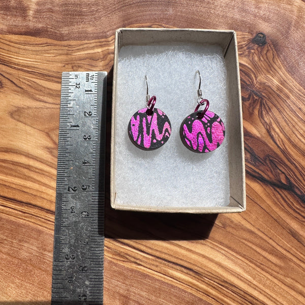 Pink and black patterned earrings in a box with a ruler for scale on a wooden surface
